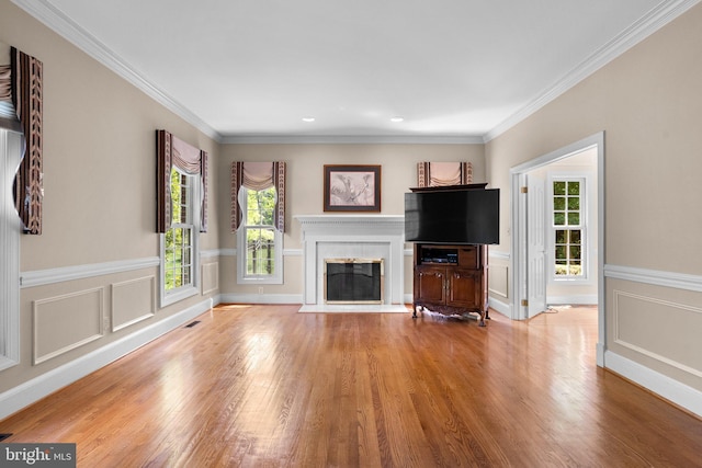unfurnished living room featuring a fireplace with flush hearth, wood finished floors, ornamental molding, and a wainscoted wall