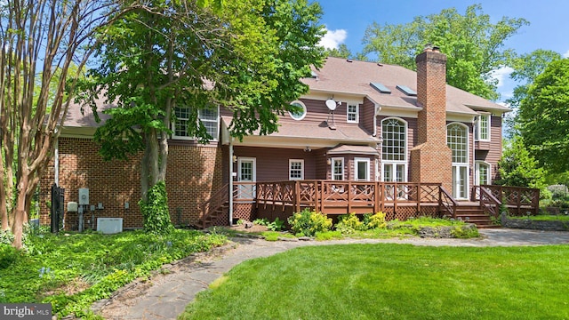 rear view of house featuring a lawn, a wooden deck, and a chimney