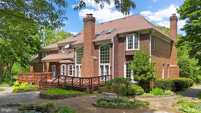 back of house with brick siding, a deck, and a chimney