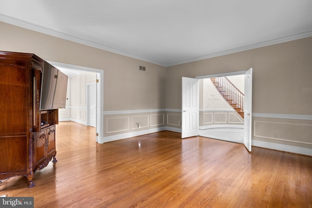 empty room featuring crown molding, stairway, light wood-type flooring, and visible vents