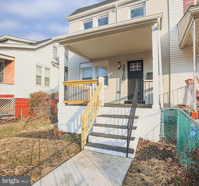 doorway to property with fence, covered porch, and brick siding