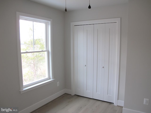 unfurnished bedroom featuring light wood finished floors, baseboards, and a closet