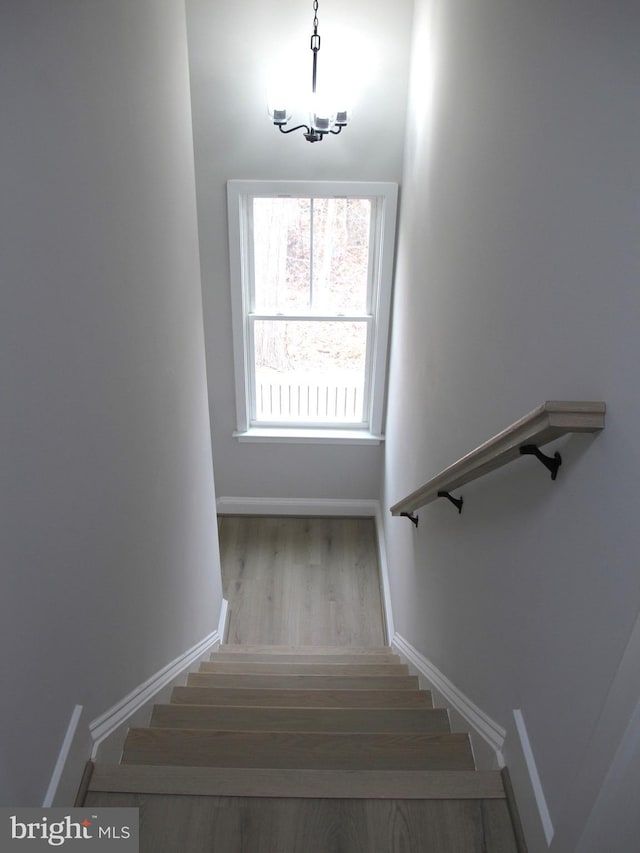 stairway featuring baseboards, a notable chandelier, and wood finished floors