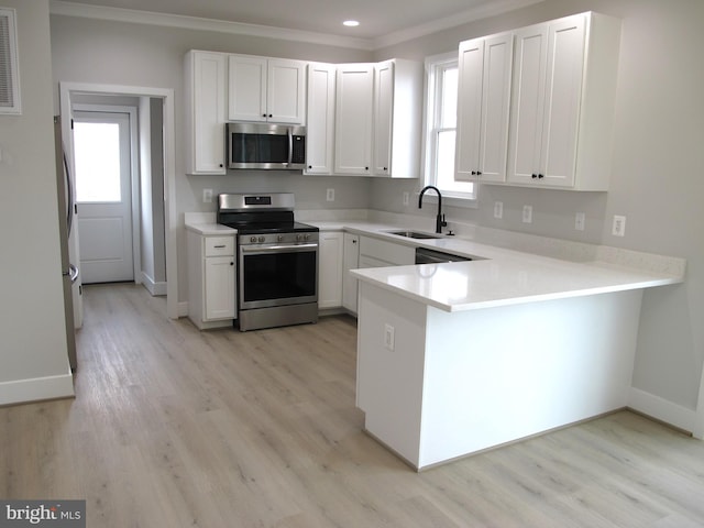 kitchen featuring light wood-type flooring, ornamental molding, a sink, a peninsula, and appliances with stainless steel finishes