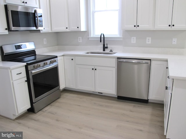 kitchen with a sink, white cabinets, light wood-style flooring, and appliances with stainless steel finishes