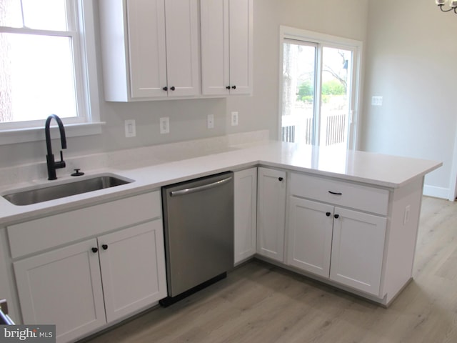 kitchen featuring white cabinets, a sink, dishwasher, light wood-style flooring, and a peninsula