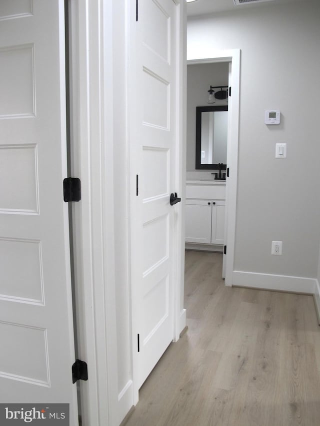hall featuring baseboards, a sink, and light wood-style floors