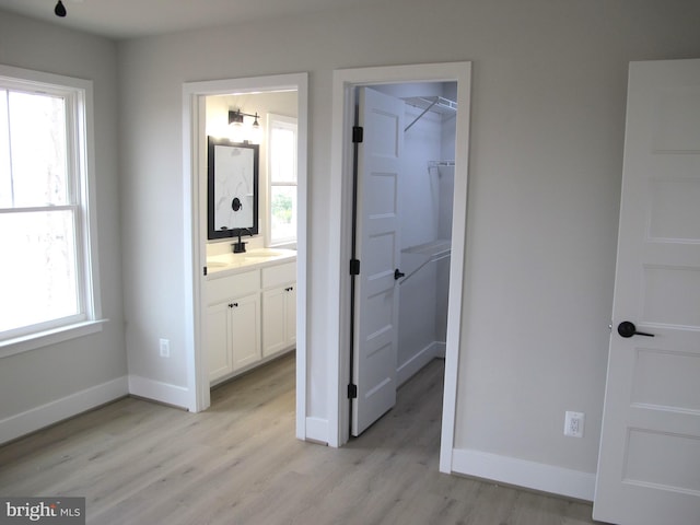 unfurnished bedroom featuring a closet, a spacious closet, ensuite bathroom, baseboards, and light wood-style floors