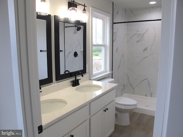 full bath with double vanity, toilet, a sink, and a marble finish shower