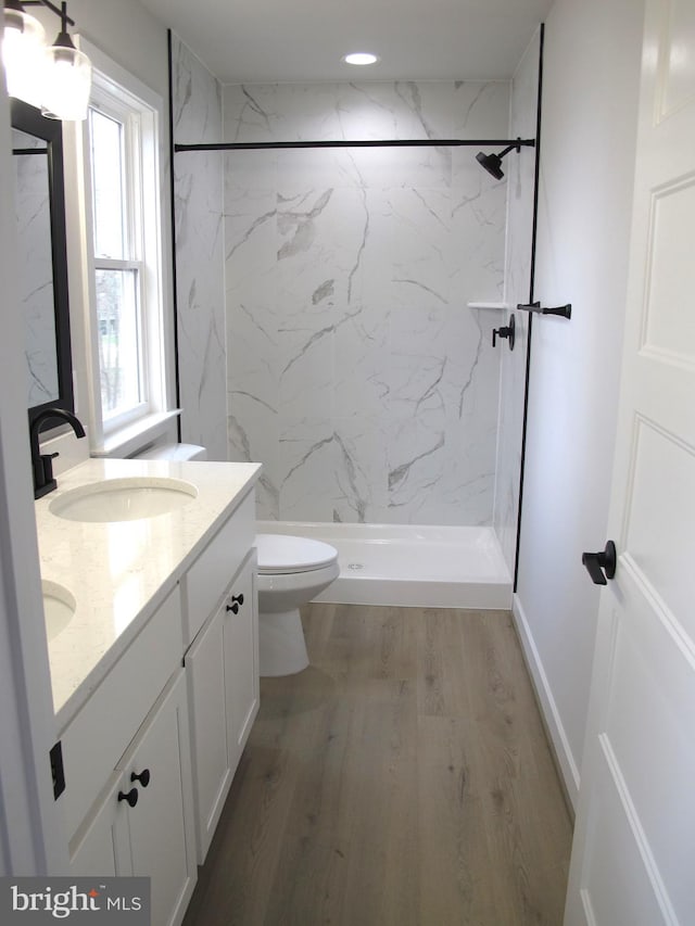 bathroom with a marble finish shower, toilet, a sink, double vanity, and wood finished floors
