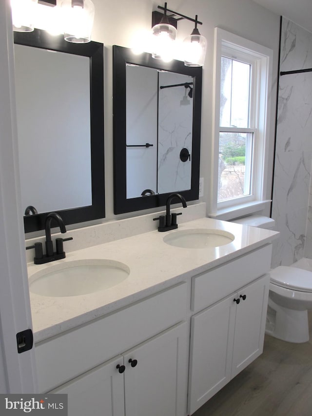 full bathroom with a marble finish shower, toilet, a sink, and double vanity