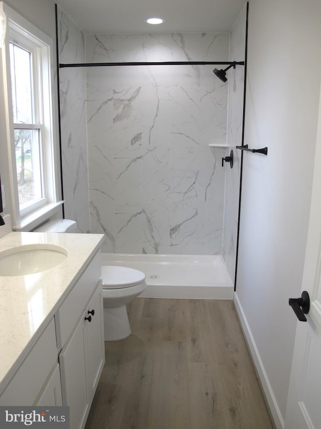 bathroom with toilet, vanity, a shower stall, wood finished floors, and baseboards