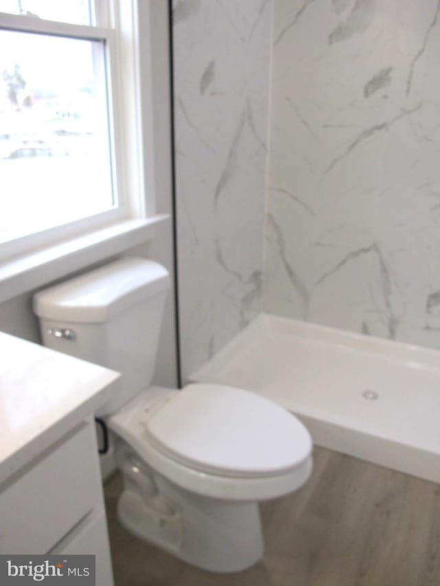bathroom featuring a marble finish shower, toilet, vanity, and wood finished floors
