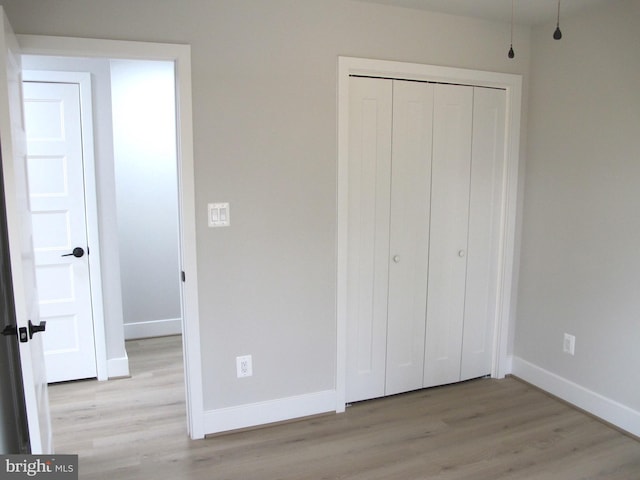 unfurnished bedroom featuring a closet, baseboards, and light wood-style floors
