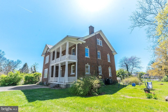 view of home's exterior with cooling unit, a chimney, brick siding, a lawn, and a balcony