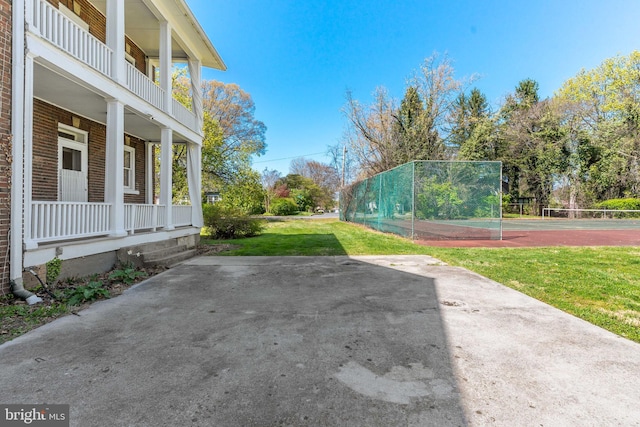 view of yard with a porch, a tennis court, and a balcony