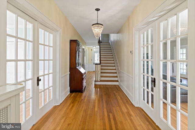 interior space featuring a decorative wall, stairs, an inviting chandelier, french doors, and light wood finished floors