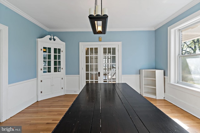 unfurnished dining area featuring ornamental molding, french doors, wood finished floors, and a wainscoted wall