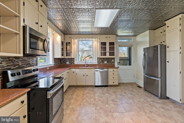 kitchen with a sink, cream cabinetry, appliances with stainless steel finishes, and an ornate ceiling