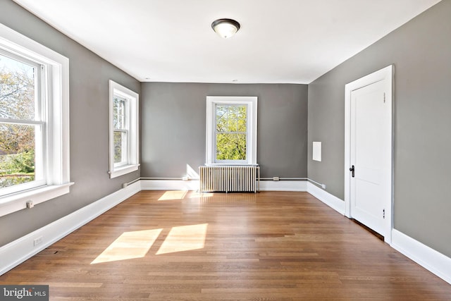 spare room with radiator heating unit, baseboards, and wood finished floors