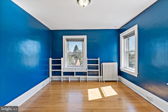 unfurnished room featuring radiator heating unit, baseboards, and wood finished floors