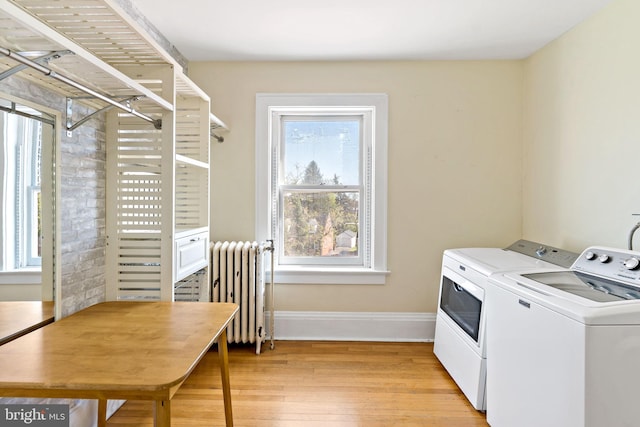 clothes washing area featuring washing machine and clothes dryer, radiator heating unit, light wood-type flooring, baseboards, and laundry area