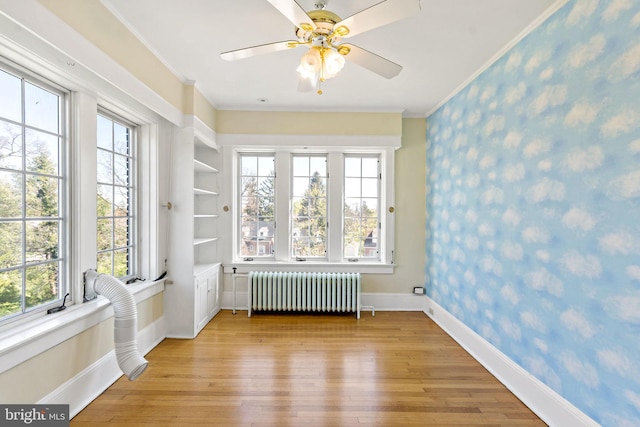 interior space featuring radiator, a wealth of natural light, crown molding, and light wood-type flooring