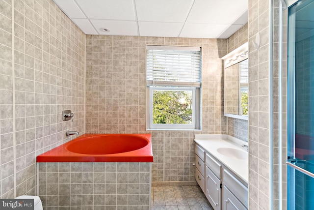 full bath featuring tile patterned floors, vanity, tile walls, a paneled ceiling, and a garden tub