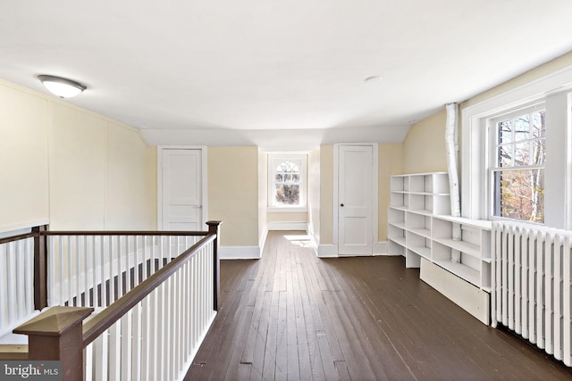 hallway featuring dark wood finished floors, radiator heating unit, an upstairs landing, and plenty of natural light