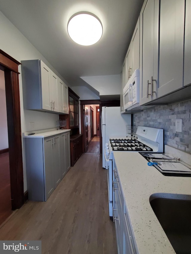 kitchen featuring a sink, wood finished floors, backsplash, and white appliances