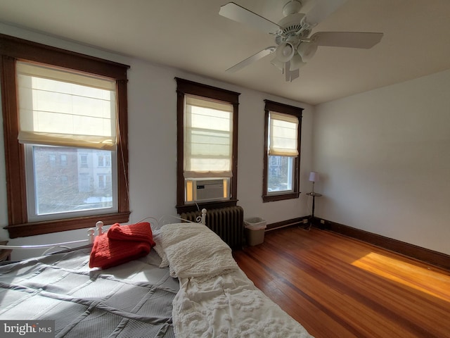 bedroom with a ceiling fan, cooling unit, wood finished floors, radiator heating unit, and baseboards