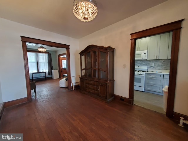 unfurnished dining area featuring dark wood-type flooring, baseboards, and an inviting chandelier