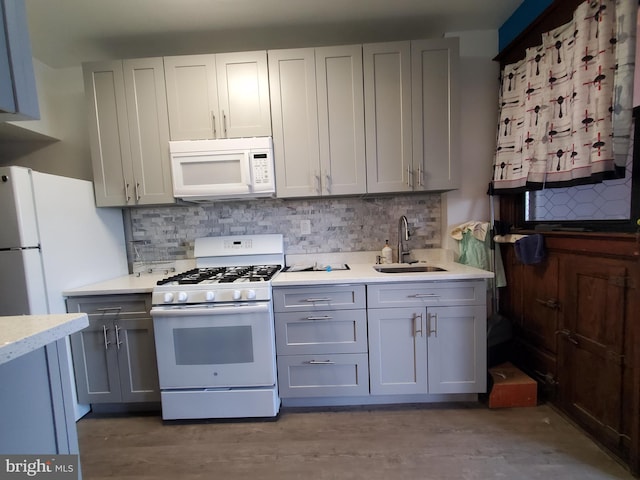 kitchen featuring a sink, gray cabinets, backsplash, and white appliances