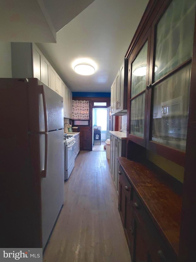 kitchen with light wood finished floors, white appliances, and white cabinetry