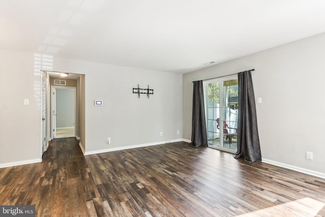 empty room featuring visible vents, baseboards, and dark wood-type flooring