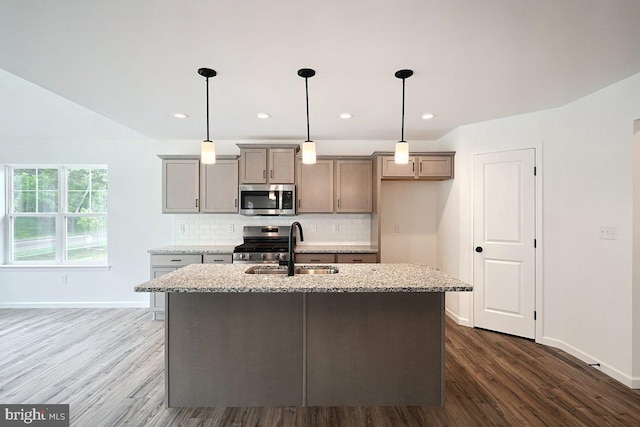 kitchen with a sink, dark wood-style flooring, appliances with stainless steel finishes, a center island with sink, and decorative backsplash