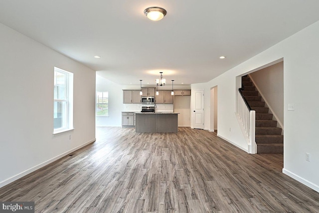 unfurnished living room featuring wood finished floors, recessed lighting, baseboards, and stairway