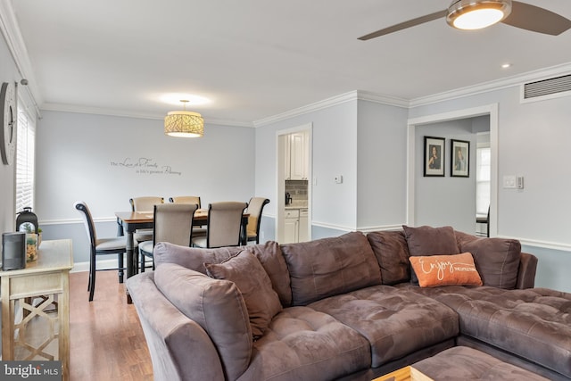 living area with baseboards, light wood-type flooring, a ceiling fan, crown molding, and visible vents