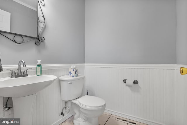 bathroom featuring tile patterned floors, toilet, and a wainscoted wall