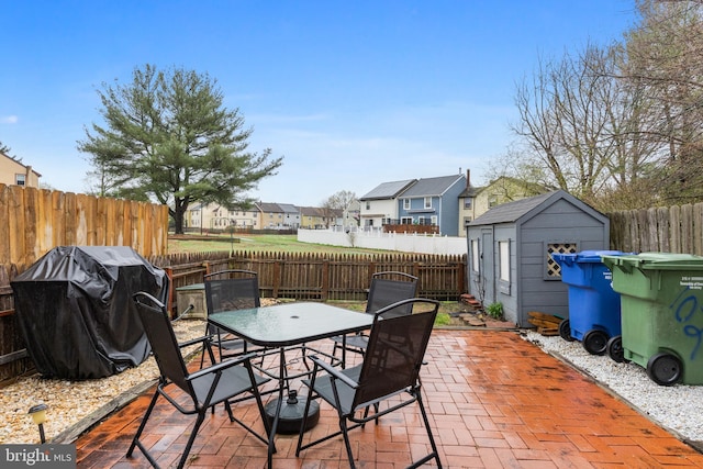view of patio with a grill, outdoor dining area, a fenced backyard, an outbuilding, and a storage unit