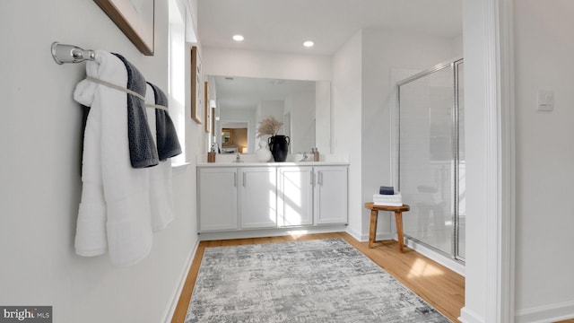 full bathroom with a shower stall, wood finished floors, double vanity, baseboards, and recessed lighting