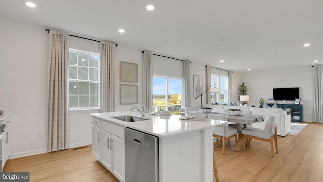 kitchen featuring a sink, stainless steel dishwasher, open floor plan, light wood-type flooring, and a kitchen island with sink