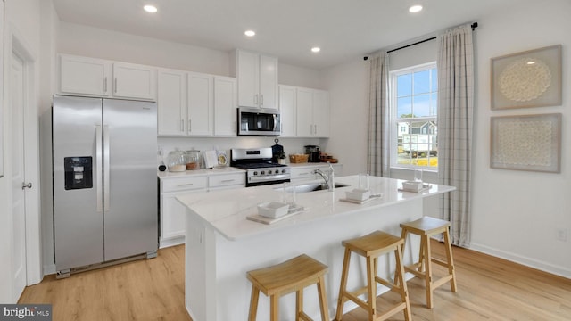 kitchen with white cabinets, light wood-style flooring, a breakfast bar, stainless steel appliances, and a sink