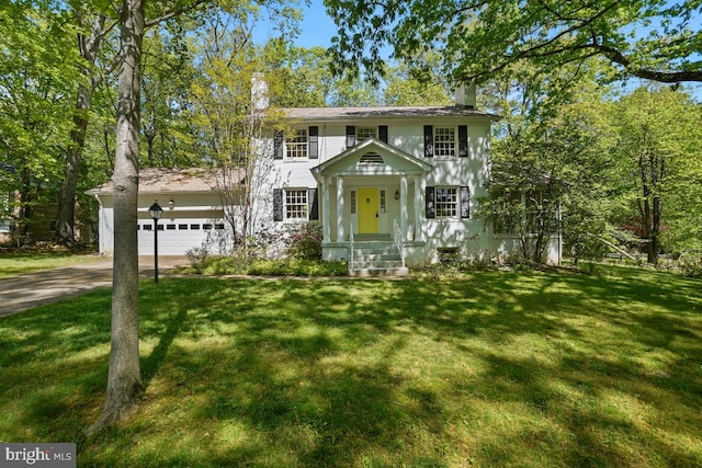 colonial-style house featuring driveway, a chimney, and a front yard