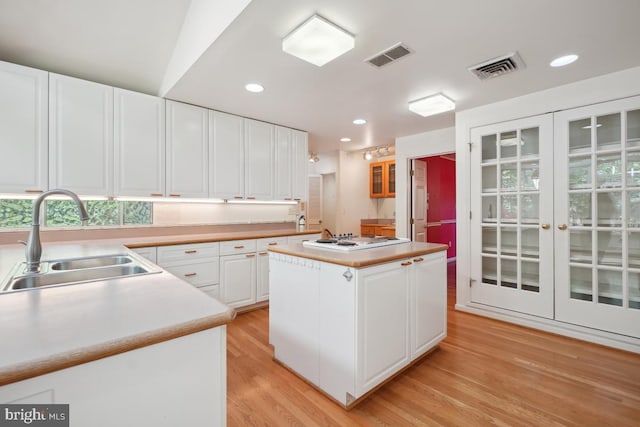 kitchen featuring visible vents, white stovetop, french doors, a sink, and light wood finished floors
