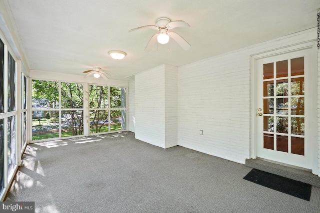 unfurnished sunroom with a ceiling fan, carpet flooring, and brick wall