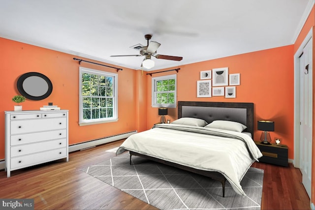 bedroom with ceiling fan, visible vents, baseboard heating, wood finished floors, and baseboards