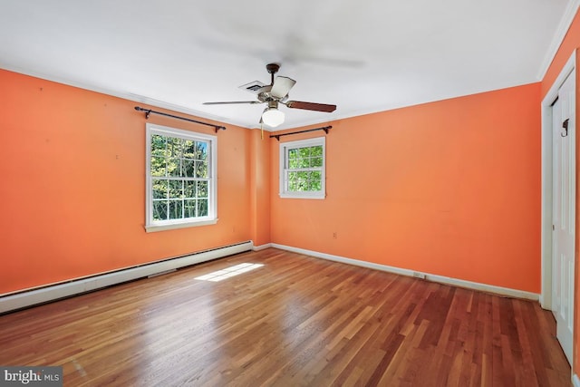 spare room with visible vents, a ceiling fan, baseboards, wood finished floors, and a baseboard heating unit