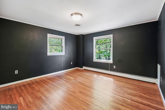 empty room featuring a healthy amount of sunlight, a baseboard heating unit, wood finished floors, and visible vents
