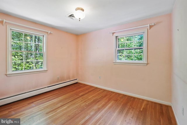 empty room featuring a healthy amount of sunlight, baseboards, baseboard heating, and wood finished floors